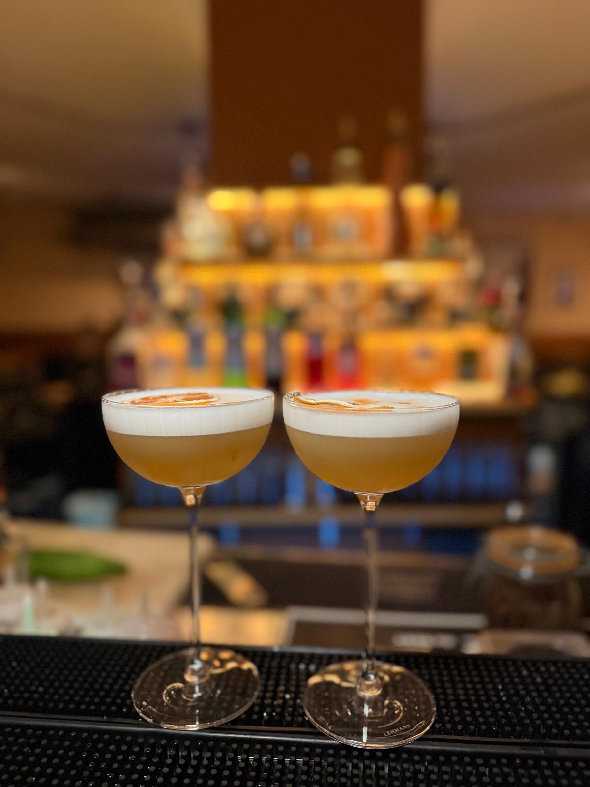 Deux cocktails signatures en coupe devant le back-bar éclairé